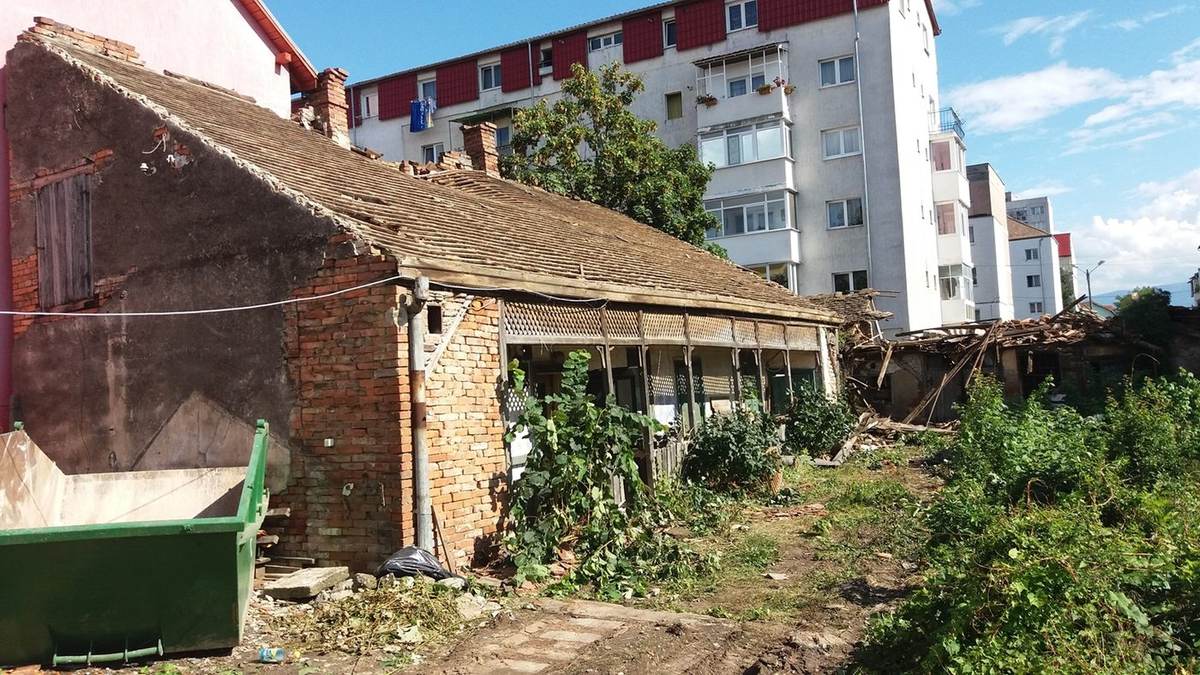 Before: single-storey brick house with tiled roof and porch, green rubble skip on site