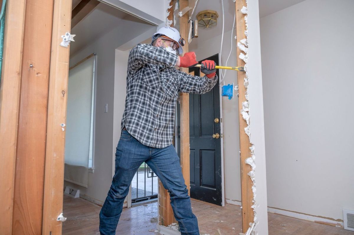 Worker removing plasterboard with a crowbar before a renovation (illustrative image)
